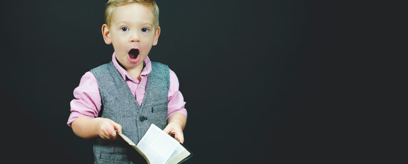 boy wearing gray vest and pink dress shirt holding book